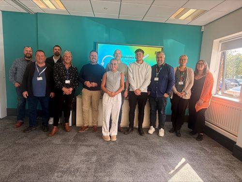 A group of people stood in a bright office boardroom smiling.
