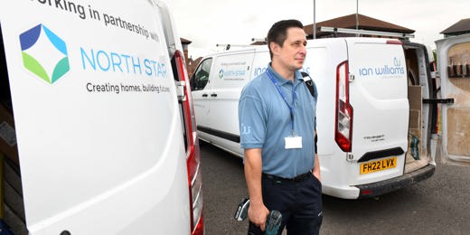A repair worker stands between two branded vans from Ian Williams and North Star Housing. He is holding tools and wearing a blue uniform and lanyard. The vans display the logos and partnership between Ian Williams and North Star Housing.