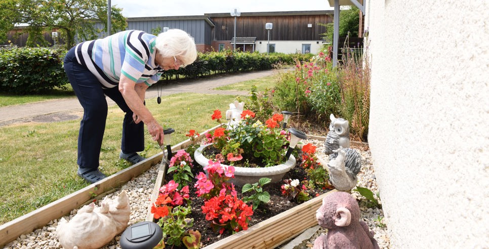 A woman tends to a flower bed surrounded by flowers and garden ornaments.