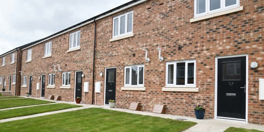 A row of terraced houses with light brick, black door and a lawn in front of the door.
